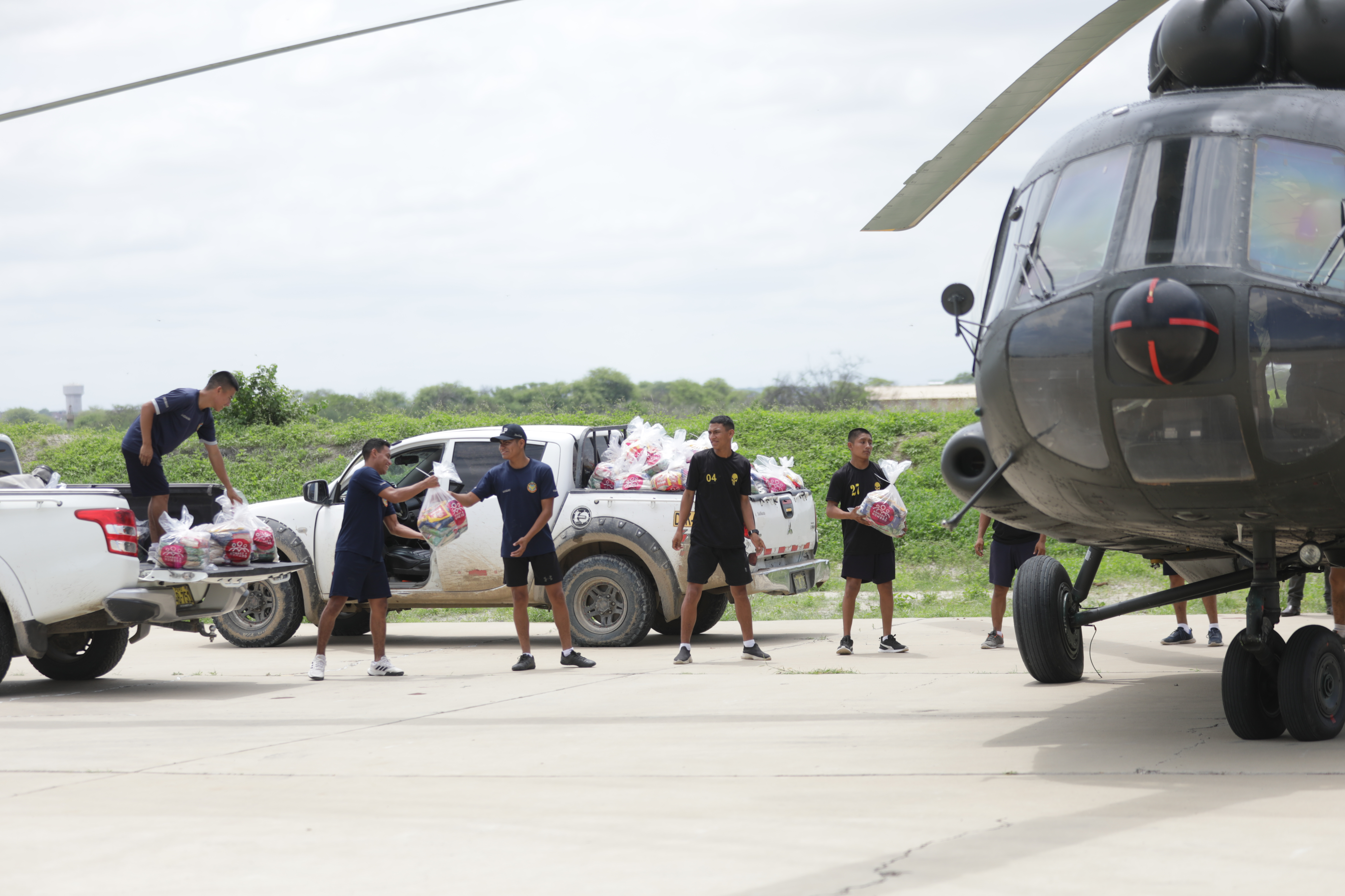 Young men in black uniforms form a line between a chopper and pickup trucks, passing bags of humanitarian aid to each other to load up the trucks.