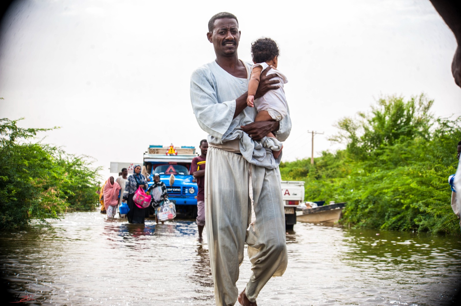 Man holding child with flooding in backdrop. Photo Credit: OCHA/Fayez Abu Bakr