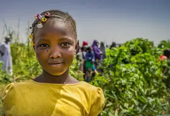 A little girl smiles to the camera in front of a crop field in Mali