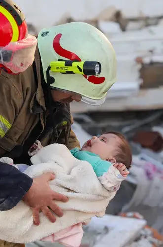 A baby is being pulled out of the earthquake rubble by two search and rescue volunteers. 