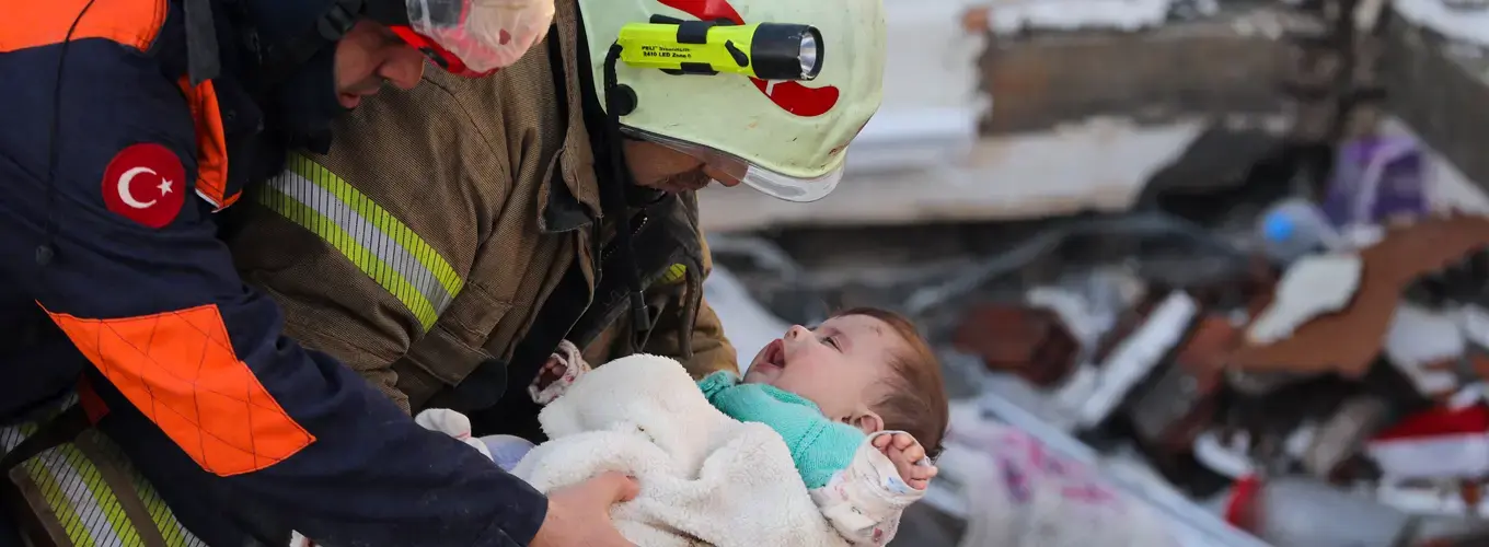 A baby is being pulled out of the earthquake rubble by two search and rescue volunteers. 